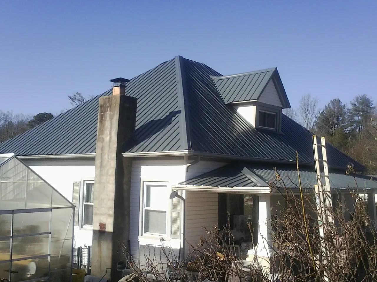 Dark blue standing seam metal roof on a white farmhouse with dormer — Slate & Tile Roof Repair by Roofing Brothers in Clay Center