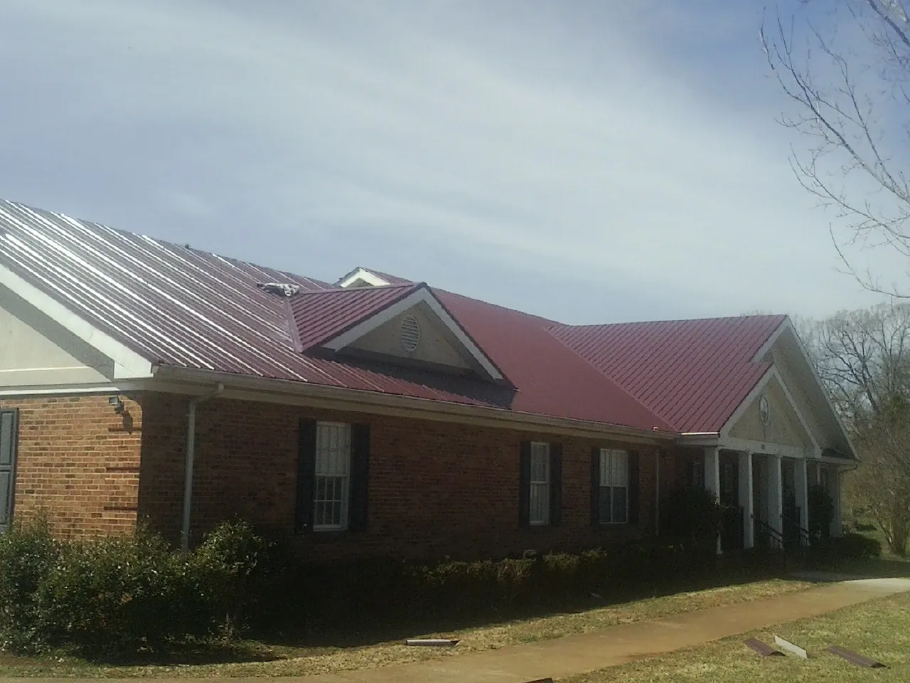 Red metal roof with gabled entries on a long brick building, from a Hail Damage Roof Repair job in Clay Center