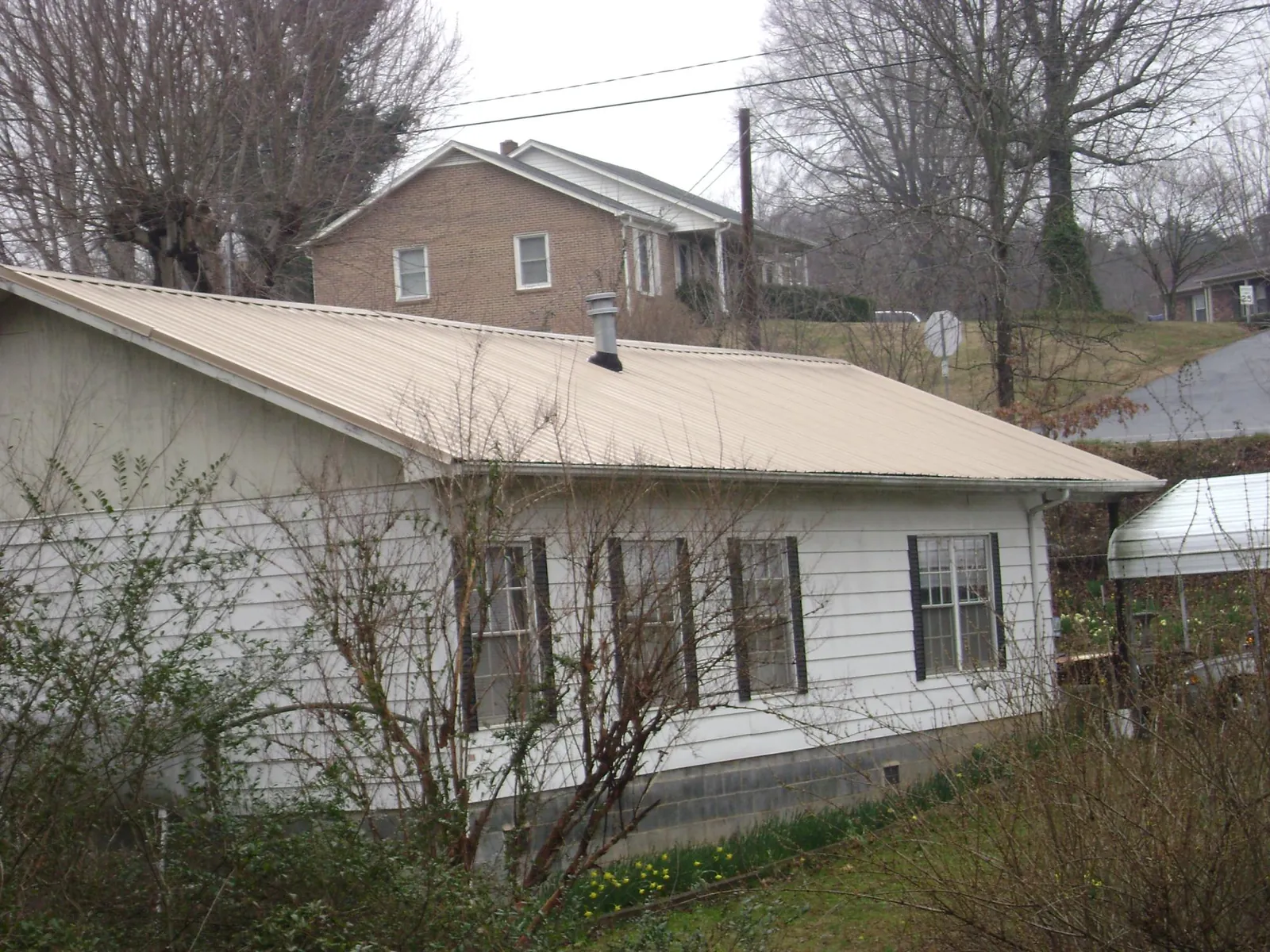 Tan metal roof on a white sided house set into a hillside — Commercial Roofing by Roofing Brothers in Clay Center